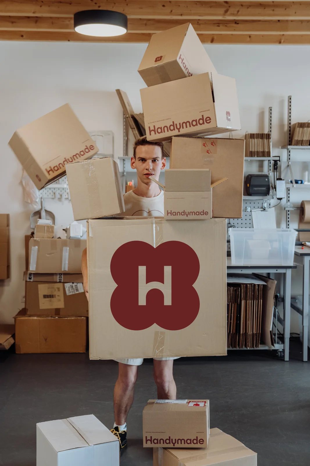 Ein Mitarbeiter aus dem Versand hält einen großen Karton mit dem Handymade-Logo, um ihn herum fallen weitere Kartons