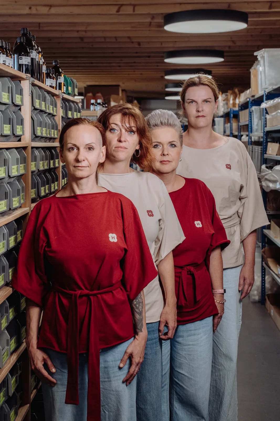 Vier Menschen aus dem Handymade-Team stehen hintereinander in einem Lagergang zwischen Regalen mit Rohstoffen