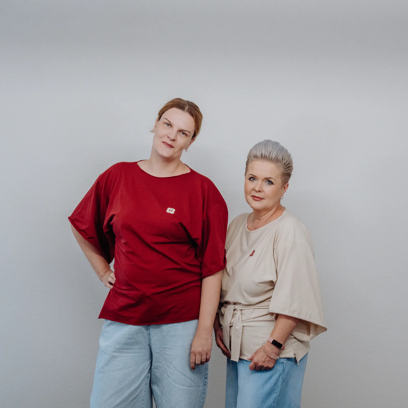 Zwei Menschen aus dem Handymade-Team in bordeauxrotem und cremefarbenem T-Shirt stehen nebeneinander vor einer grauen Wand