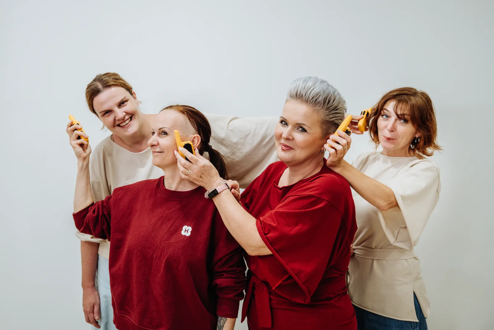 Vier Menschen aus dem Handymade-Team in bordeauxroten und cremefarbenen T-Shirts lachen und halten gelbe Funkgeräte ans Ohr